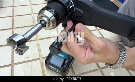 A close up view of hands holding a modern cordless power drill with a large wood boring bit attached. Stock Photo