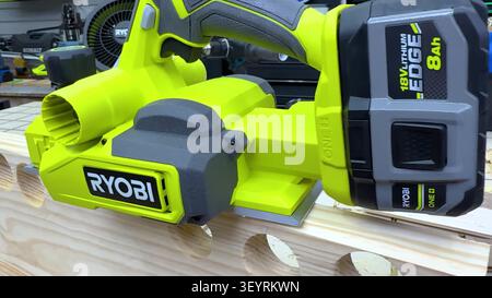 A lime green and grey cordless electric hand planer rests on a wooden board with drill holes. Stock Photo