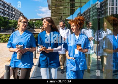 Medical professionals walking outside hospital building smiling together Stock Photo