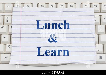 Lunch and Learn text on ripped lined paper on a white computer keyboard for online courses and e-learning Stock Photo