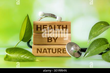 Alternative medicine and organic healthcare concept with stethoscope, green leaves and wooden blocks with text HEALTH BY NATURE, natural green backgro Stock Photo