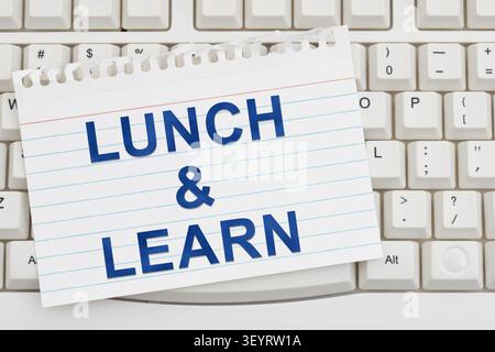 Lunch and Learn text on ripped lined paper on a white computer keyboard for online courses and learning Stock Photo