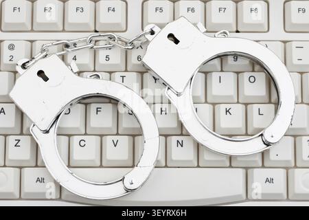 Handcuffs on a white computer keyboard for computer forensics of identity theft, Stock Photo