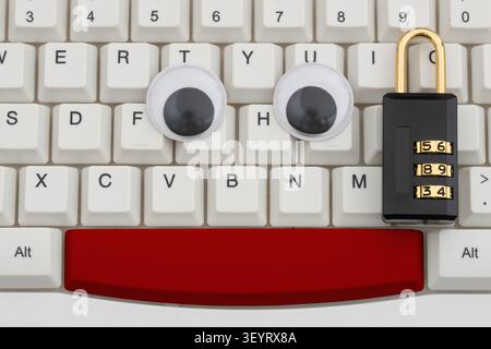Googly eyes with combination lock on a white computer keyboard for privacy protection Stock Photo