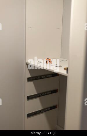 A white server cabinet features an open shelf with orange connectors, cables, and small tools. Three horizontal server blade rails are mounted below t Stock Photo