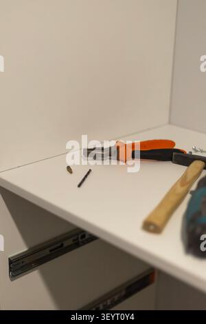 Orange handled pliers and various hardware tools resting on a white desk. Detailed view of metal hardware and a screwdriver handle in a workspace sett Stock Photo