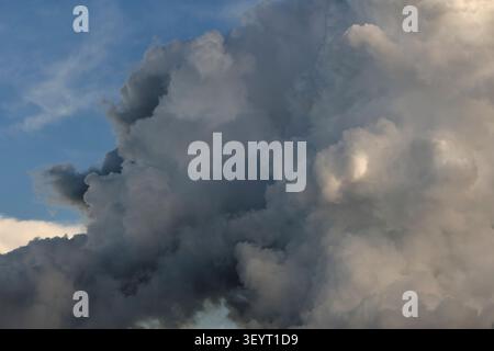 Dense heavy storm clouds with dark shadows and bright white edges cover entire blue sky background Stock Photo