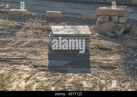 Concrete slabs neatly stacked on an uneven ground, featuring construction debris, bricks, and sunlight casting clear shadows in an active outdoor sett Stock Photo