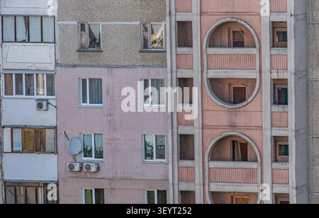 Multi-story residential building in urban setting, featuring muted pink facade and concrete texture, standard rectangular windows with varying states Stock Photo