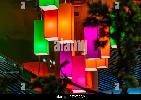 Interior design featuring hanging rectangular light fixtures, vibrant colors, dark textured wall, blurred foliage elements, warm inviting glow, contem Stock Photo