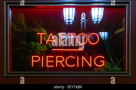 Red neon "Tattoo Piercing" sign glowing in the shop window of a tattoo studio at night in Berlin, Germany. Stock Photo