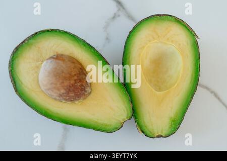 avocado halves sliced open on marble surface fresh and natural top-down perspective seed food photography healthy eating green yellow commercial light Stock Photo