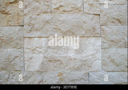 Close-up of a natural stone wall with rectangular beige stone blocks forming a clean architectural texture. Detailed surface pattern with subtle color Stock Photo