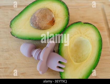 Avocado sliced and cut in half, in wooden cutting board, with avocado, cutting board, pink avocado cutter, with wood, plastic texture, from a top-down Stock Photo