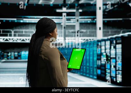 Data center administrator works with a chroma key tablet, using an editable screen to track performance metrics. Stock Photo