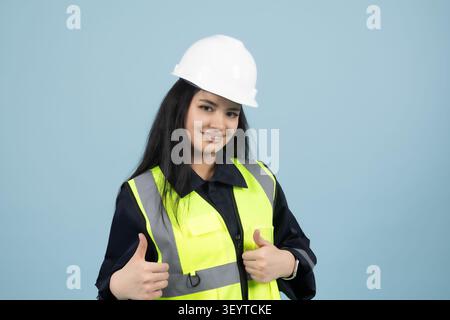 Female engineer wearing hard hat smiling confidently in studio with blue Stock Photo