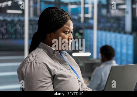 African American engineer uses a notebook to oversee data center machines, maintain server rigs and solve complex workloads. Stock Photo
