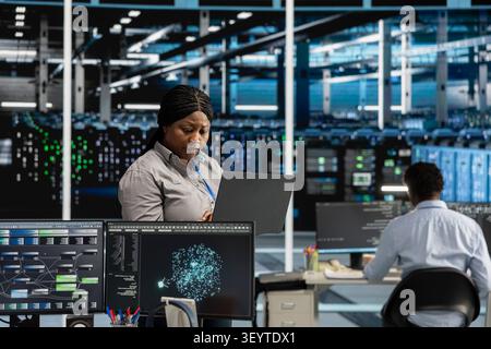 African American woman uses AI visualization tools in a server hub to find errors, read insights and detect hardware failures. Stock Photo