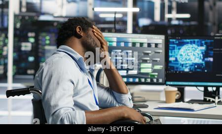 Engineer using a wheelchair reacts to a slow AI node tree tool while working in a data center. Stock Photo