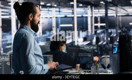 Data center technician monitors operational metrics on digital device inside a server room to improve infrastructure performance. Stock Photo