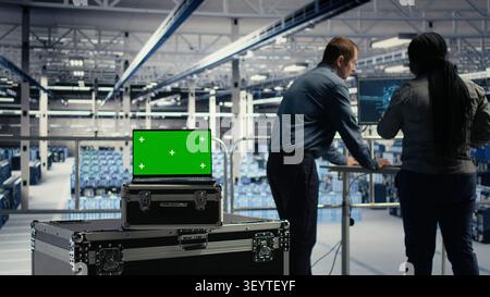 Programmers use green screen laptop in a data center to upgrade server hardware and improve workload capacity. Stock Photo
