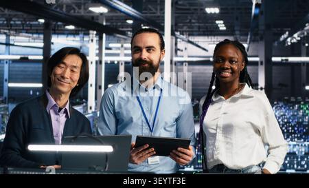 Smiling engineers in a server room review AI diagnostics and performance data together. Stock Photo