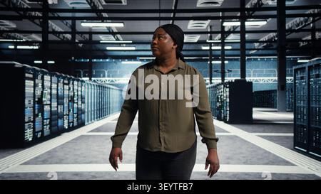 Software engineer walking in server facility, checking hardware for system stability. IT administrator supervising server environment room, checking infrastructure systems. Stock Photo