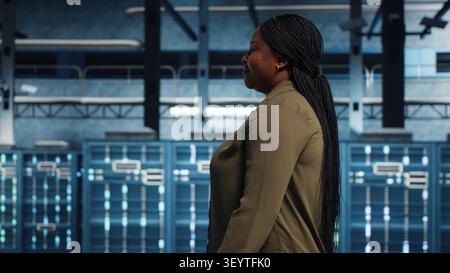 IT administrator working in server facility to optimize network infrastructure. African American woman in in server environment diagnosing and resolving hardware malfunctions working with device. Stock Photo