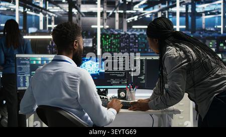 Server room supervisor overseeing work done by engineer working with deep learning models to review data sets. Stock Photo