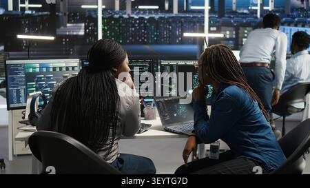 Server facility coworkers discussing ideas, applying AI ML models to set up equipment. IT experts cooperating in server environment, working on optimizing systems. Stock Photo