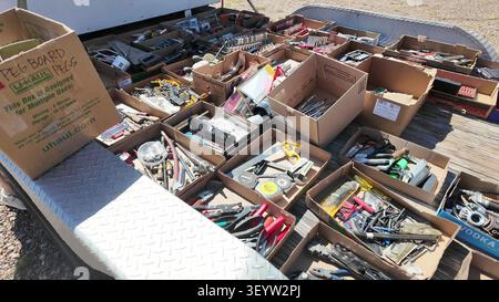 Various cardboard boxes filled with categorized hand tools, hardware, and equipment arranged on a trailer bed at an outdoor sale. Stock Photo