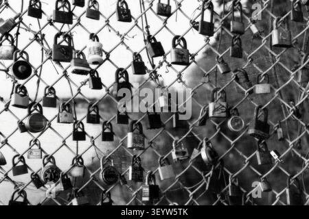 Black and white close-up of numerous love padlocks attached to a chain-link fence symbolizing romance and everlasting love Stock Photo