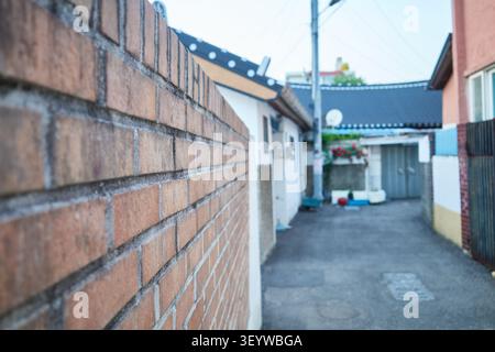 Quiet residential alleyway with a textured brick wall and vibrant pink blossoms. Nostalgic spring urban landscape capturing vintage neighborhood charm Stock Photo