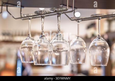 Clear empty wine glasses hanging upside down on a metal rack in a modern restaurant interior Stock Photo