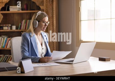 Businesswoman holding papers during videocall, reviewing document, communicating with colleagues Stock Photo