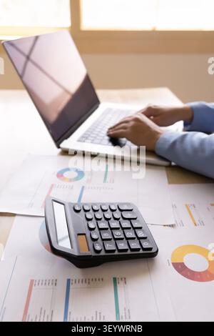 Female bookkeeper typing on laptop at desk with financial documents Stock Photo