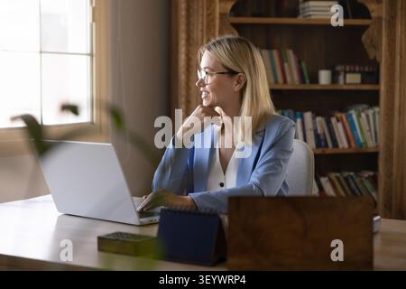 Smiling woman working on laptop in home office Stock Photo