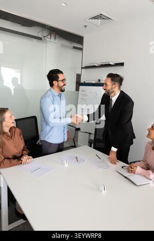 Two businessmen shake hands during group meeting in conference room Stock Photo