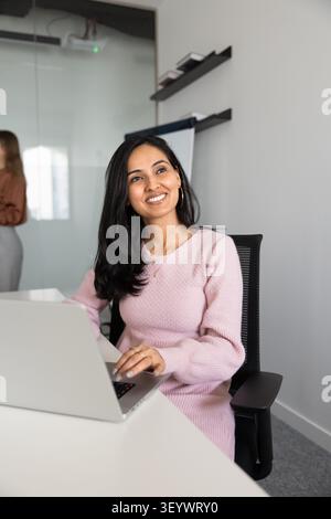 Smiling Indian female professional sitting at desk with laptop Stock Photo