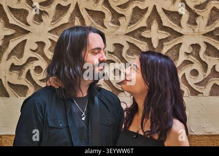 Close-up portrait of a young couple looking at each other against a decorative patterned wall. Stock Photo