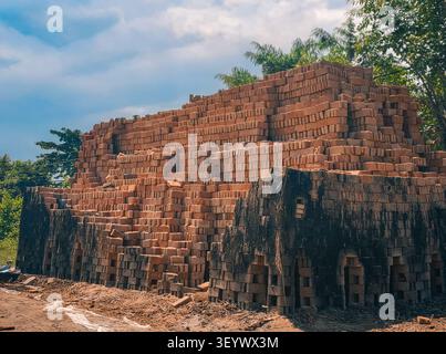A large stack of traditional red bricks arranged for firing or drying in an outdoor brickyard under a blue sky. Stock Photo