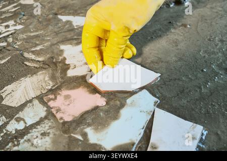 Hand in yellow rubber glove placing ceramic pieces into wet cement for mosaic. Upcycling old materials Stock Photo
