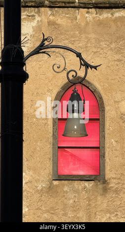 Vintage street lamp mounted on a weathered stone wall beside an arched window with vibrant red glass panes. The ornate metalwork and architectural ele Stock Photo