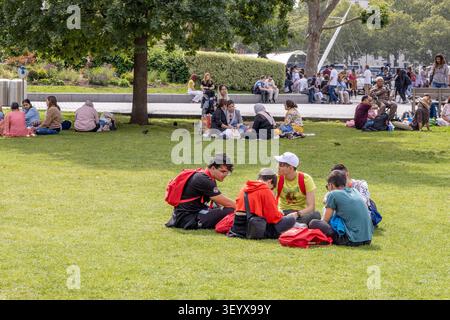 Group of young friends sitting on green grass in a city park. London, UK, 23 July 2023 Stock Photo