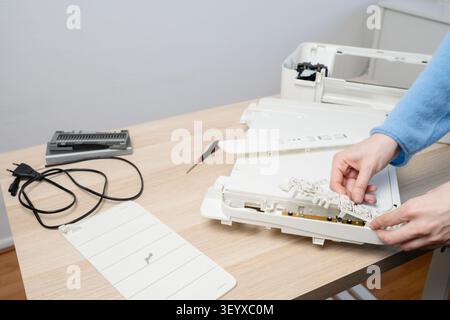 Hands of a technician disassembling a flatbed scanner printer on a wooden desk with tools, cables and spare parts, illustrating office equipment repai Stock Photo