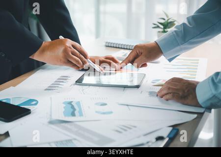 Business professionals analyzing financial charts on smartphone with printed reports, calculator and documents on office desk, showing investment plan Stock Photo