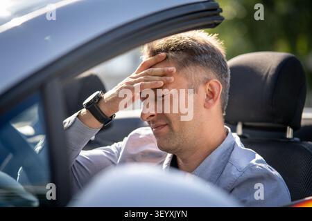 Mature man experiencing stress, headache, and frustration in a convertible car. headache while driving. The businessman is tired of working and standi Stock Photo