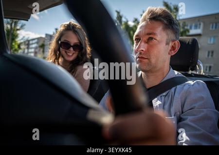 a young couple traveling together by car. Happy couple talking and smiling while driving in a convertible car. Summer road trip, romance, and joyful l Stock Photo