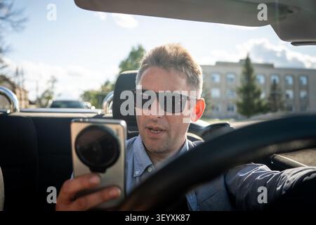 Young driver looking at her smartphone while holding the steering wheel. Distracted driving and dangerous road navigation. the driver is distracted by Stock Photo