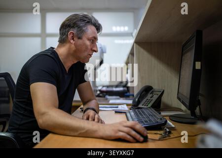 Office worker looking intently at a computer monitor while using a mouse at his desk. Focused work, data analysis, and IT tasks. Stock Photo
